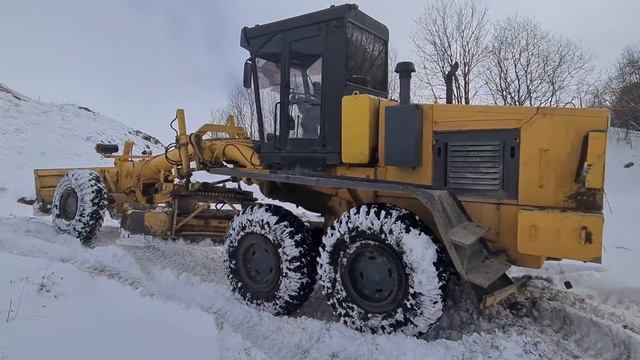 Грейдер на заснеженной дороге в горах.