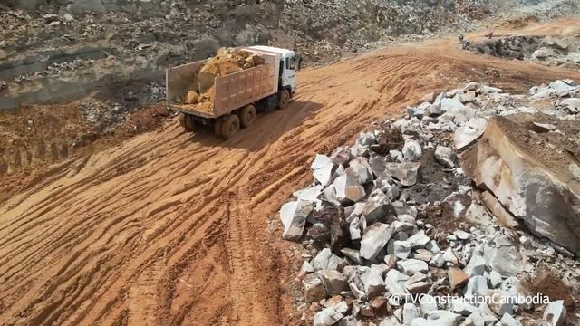 фундамент здания на горной дороге, оператор бульдозера, самосвал разгружающий камни